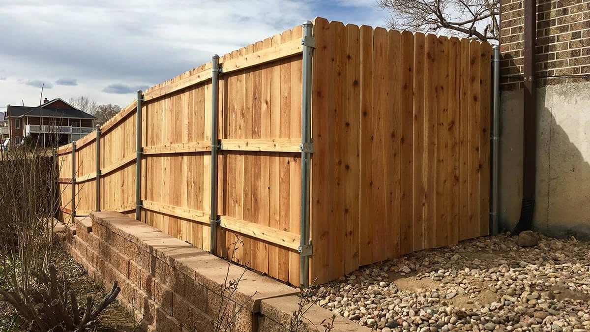 Cedar privacy fence with metal posts installed along a raised landscape edge