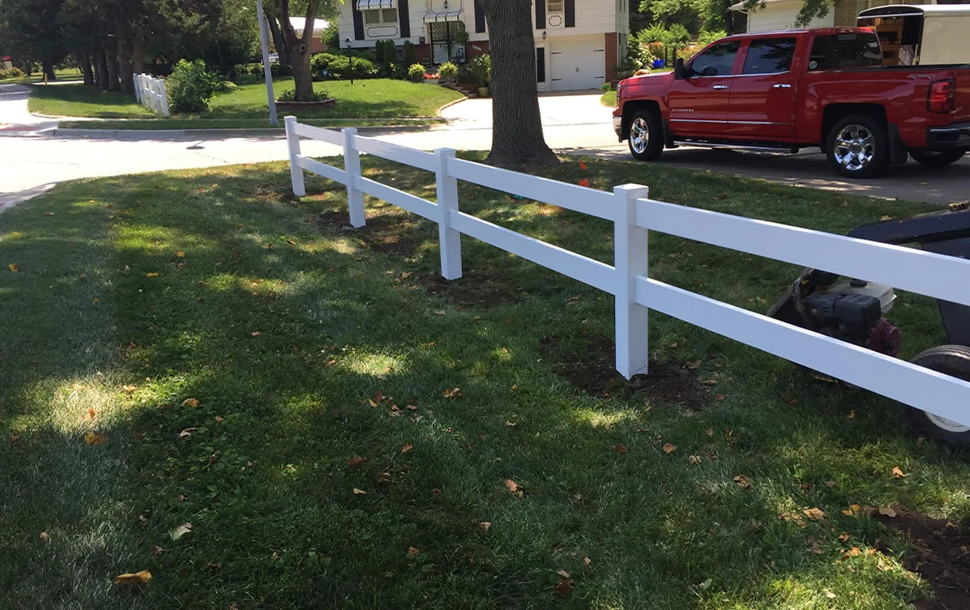 White vinyl two-rail fence installed across a residential front yard